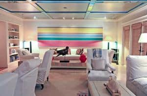 A photo of a Florida-style living room decorated with a large abstract painting by Kenneth Noland, comfortable furniture, photos and decorative objects.