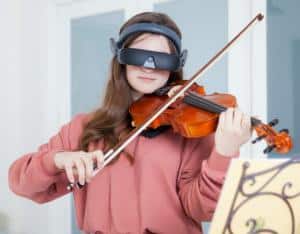 Young woman wearing eSight while viewing sheet music and playing the violin.