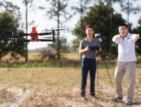 drone (in focus) at GCREC, with Dana Choi, left, and Kevin Wang in the background. Choi and Wang are both UF/IFAS assistant professors of agriculture and biological engineering at GCREC – and they’re both new faculty hires in AI.